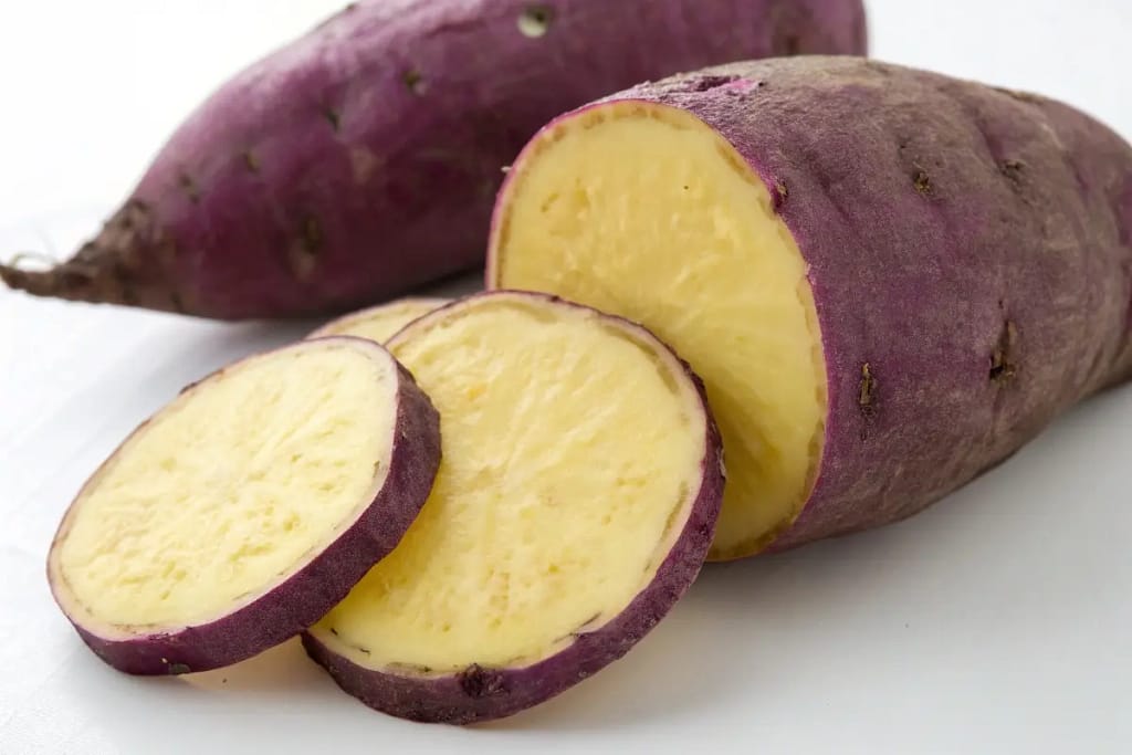 Highlighting the distinctive purple skin and pale interior of a Japanese sweet potato, key to its unique taste and dessert potential.