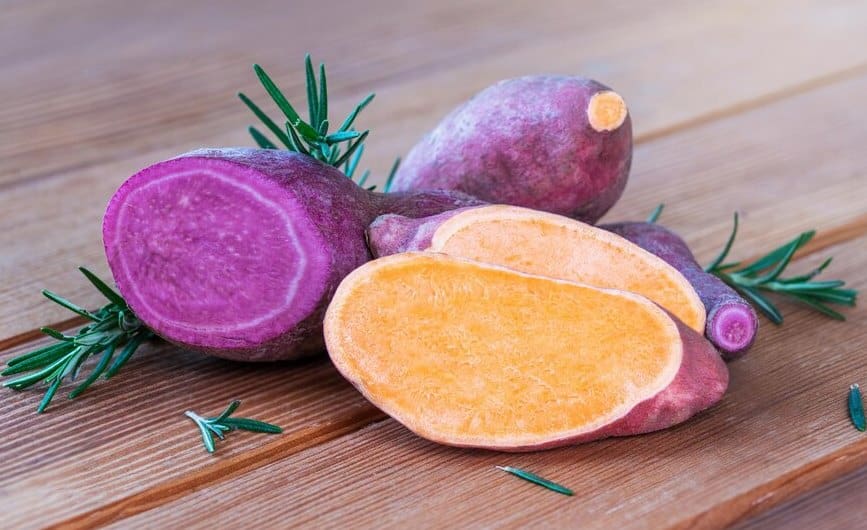 Close-up of Japanese sweet potatoes with purple skin and yellow flesh, both whole and cut pieces.